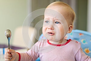 Cute adorable caucasian blond toddler boy sitting in high chair and crying while feeding. Upset unhappy child refuse to eat