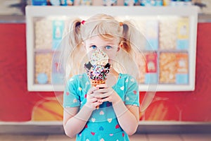 Caucasian blonde preschool girl child with blue eyes holding ice cream in large waffle cone