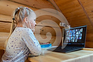 Cute adorable caucasian little blond girl siiting at desk with laptopn during online video chat scholl lesson session with teacher