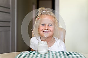 Cute adorable caucasian little funny blond girl eating yogurt or milk cottage cheese for lunch snack. Child enjoy eating