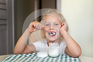 Cute adorable caucasian little funny blond girl eating yogurt or milk cottage cheese for lunch snack. Child enjoy eating