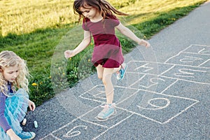Cute adorable children girls friends playing jumping hopscotch outdoors. Funny activity game for kids on playground outside.