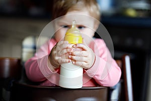 Cute adorable ewborn baby girl holding nursing bottle and drinking formula milk