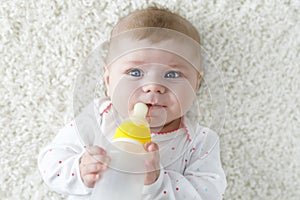 Cute adorable ewborn baby girl holding nursing bottle and drinking formula milk. First food for babies. New born child