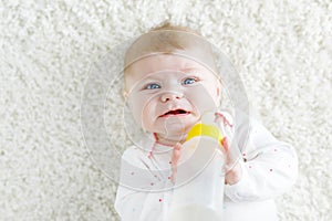 Cute adorable ewborn baby girl holding nursing bottle and drinking formula milk photo