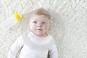 Cute adorable ewborn baby girl holding nursing bottle and drinking formula milk. New born child, little girl laying on