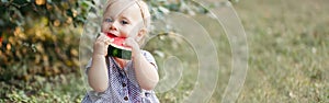 Cute adorable funny Caucasian baby girl eating ripe watermelon sitting on ground. Funny child kid with fresh red fruit outdoors in