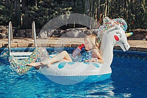 Cute adorable girl in sunglasses with drink lying on inflatable ring unicorn. Kid child enjoying having fun in swimming pool.