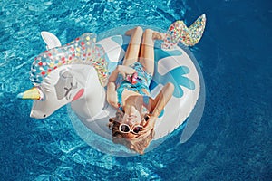 Cute adorable girl in sunglasses with drink lying on inflatable ring unicorn. Kid child enjoying having fun in swimming pool.