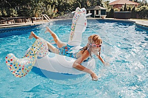 Cute adorable girl in water goggles lying chilling on inflatable ring unicorn. Kid child enjoying having fun in swimming pool.