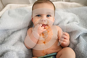 Cute adorable infant funny dirty baby trying to eat himself with fruit or vegetable puree smeared on his face. Baby