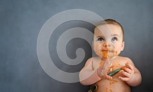 Cute adorable infant funny dirty baby trying to eat himself with fruit or vegetable puree smeared on his face. Baby