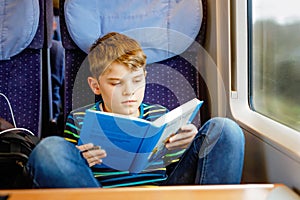 Cute adorable kid boy reading book during traveling by train. Happy child sitting near window. Family going on vacations