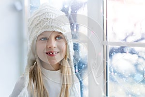 Cute adorable little blond beautiful cauasian girl stay near window, dream and looking outside waiting for snow, wonders photo