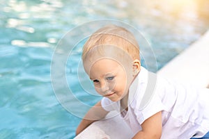 Cute adorable little caucasian blond smiling todller boy kid treing water temperature pool edge before swimming. Happy