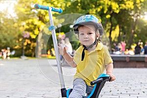 Cute adorable little caucasian toddler boy portrait in helmet having fun riding three-wheeled balance run bike scooter in city