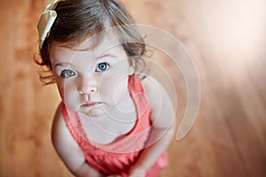 Cute, adorable and little girl standing while looking up with sweet face on wooden floor at home. Portrait of small girl