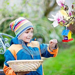Cute adorable little kid boy making an egg hunt on Easter. Happy child searching and finding colorful eggs in domestic
