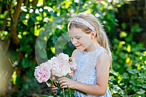 Cute adorable little preschool girl with huge bouquet of blossoming pink peony flowers. Portrait of smiling preschool