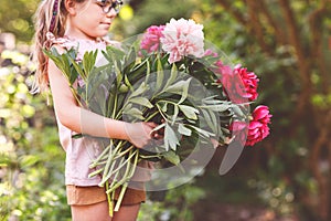 Cute adorable little preschool girl with huge bouquet of blossoming red and pink peony flowers. Portrait of smiling