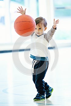 Cute adorable little small white Caucasian child toddler boy playing with ball in gym