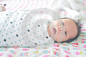 Cute adorable newborn baby boy wrapped or swaddle in a blanket, sleeping and sometime both eyes open in kids bed