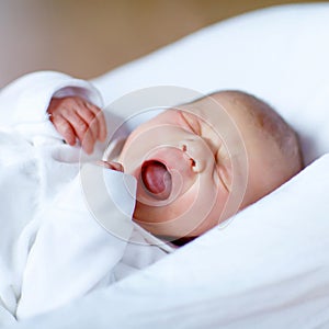 Cute adorable newborn baby crying in white bed. New born child, little girl laying in bed. Family, new life, childhood