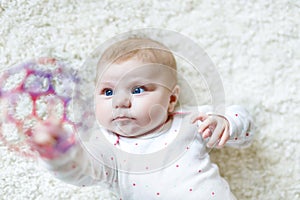 Cute adorable newborn baby playing with colorful ball toy on white background. New born child, little girl looking at