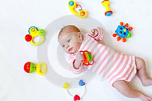 Cute adorable newborn baby playing with colorful rattle toy. in white bed at home. New born child, little girl looking