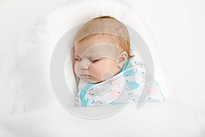 Cute adorable newborn baby wrapped in white blanket, sleeping in kids bed or cocoon. Closeup of peaceful child, little