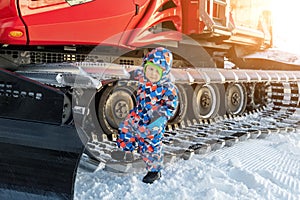 Cute adorable playful happy toddler boy play at red modern snowcat ratrack snowplow box grooming standing on peak alpine