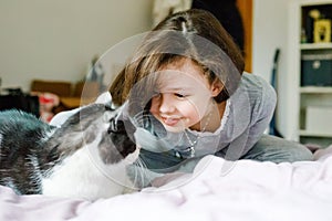 Cute adorable school kid girl cuddling and playing together with cat in bed in morning. Happy family, friendship between