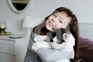 Cute adorable school kid girl cuddling and playing together with cat in bed in morning. Happy family, friendship between