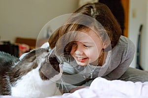 Cute adorable school kid girl cuddling and playing together with cat in bed in morning. Happy family, friendship between