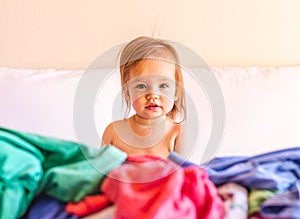 Cute, Adorable, Smiling, Caucasian Baby Sitting in a Pile of Dirty Laundry on Bed