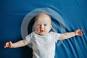 Cute adorable smiling white Caucasian baby girl boy with blue eyes four months old lying on bed in bedroom looking at camera