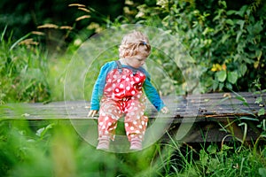 Cute adorable toddler girl sitting on wooden bridge and throwing small stones into a creek. Funny baby having fun with