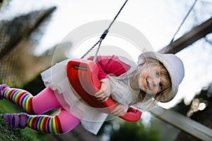 Cute adorable toddler girl swinging in domestic garden with soft plush toy. Happy healthy baby child in hat and dress