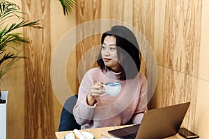 Cute adult girl plays in a laptop in a coffee shop. Asian woman working in a cafe at a laptop. Freelance concept
