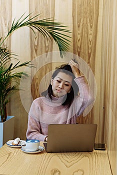 Cute adult girl plays in a laptop in a coffee shop. Asian woman working in a cafe at a laptop. Freelance concept