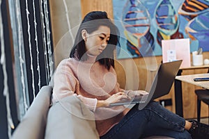 Cute adult girl plays in a laptop in a coffee shop. Asian woman working in a cafe at a laptop. Freelance concept