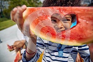 Cute african american boy folding up a piece of watermelon fruit with carved in heart and looking through the hole