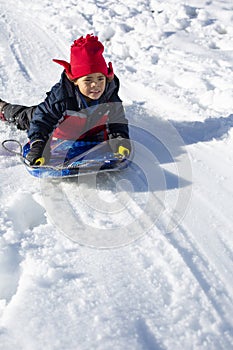 Cute African American boy sledding down the hill on a snowy day