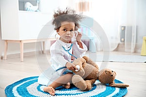 Cute African American child imagining herself as doctor while playing with stethoscope and toy bunny