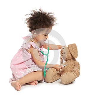 Cute African American child imagining herself as doctor while playing with stethoscope and toy bunny