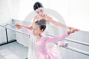 cute african american child in pink tutu exercising with teacher