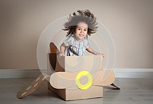 Cute African American child playing with cardboard plane near wall