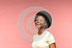 Cute African American female with beautiful afro hairstyle laughing, isolated pink studio background