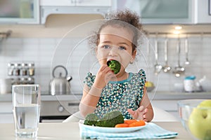 Cute African-American girl eating vegetables at table