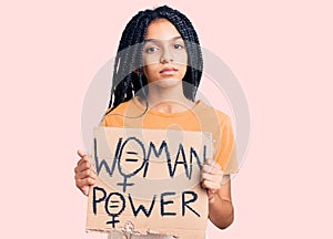 Cute african american girl holding woman power banner thinking attitude and sober expression looking self confident
